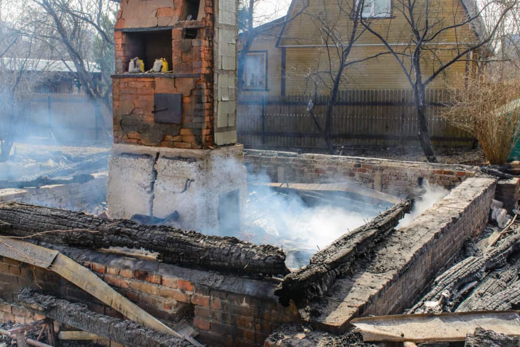 The aftermath of a house fire with only the chimney standing amidst the ruins and smoldering debris.