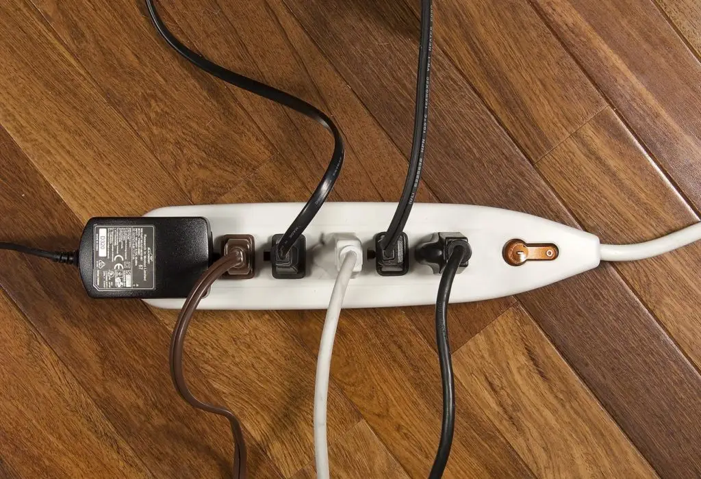 A power strip with multiple cords plugged in, showcasing a common scene of electrical connectivity and management on a wooden floor.